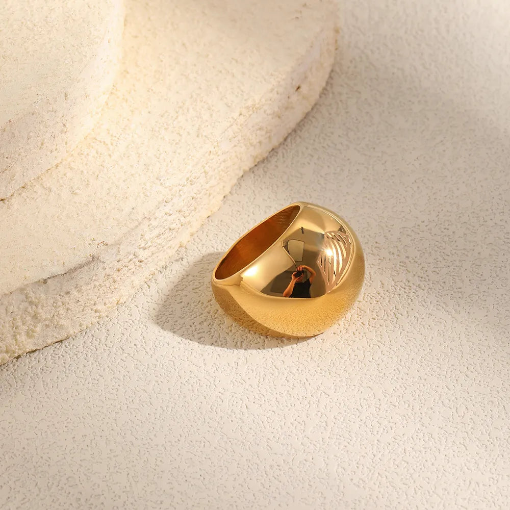 Chunky gold dome ring lying on sand beside white stone – 18K gold PVD titanium ring