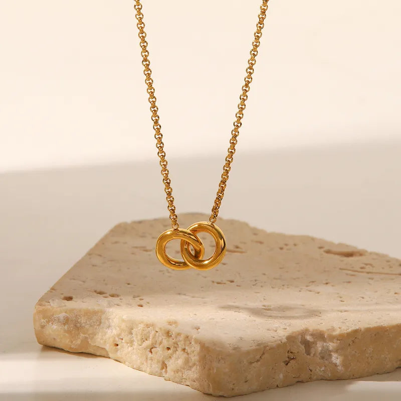 Gold interlinked rings pendant necklace hanging over travertine stone — everyday necklace The Gold Collective