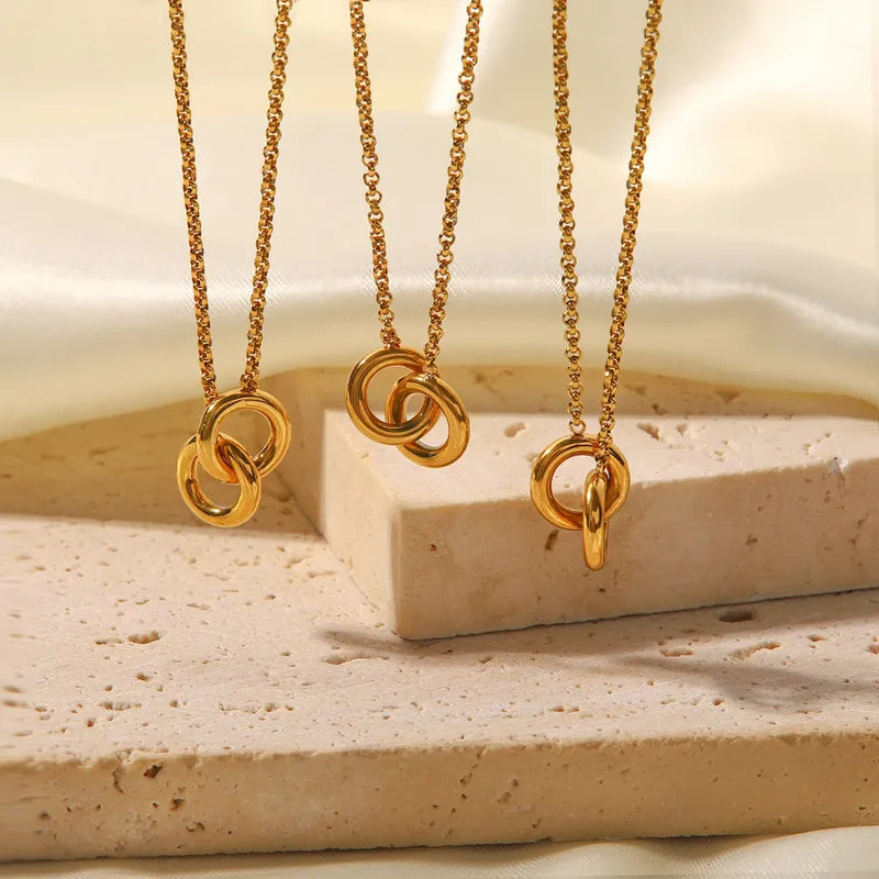 Three interlinked rings gold necklaces displayed on travertine stone — waterproof titanium necklace South Africa